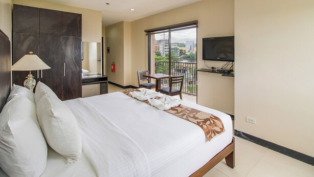Une chambre d’hôtel équipée d’un lit, d’un bureau, d’une chaise, d’une télévision et d’un balcon avec vue sur la ville.