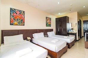 Habitación de hotel con tres camas, un escritorio, un armario y dos cuadros en la pared.