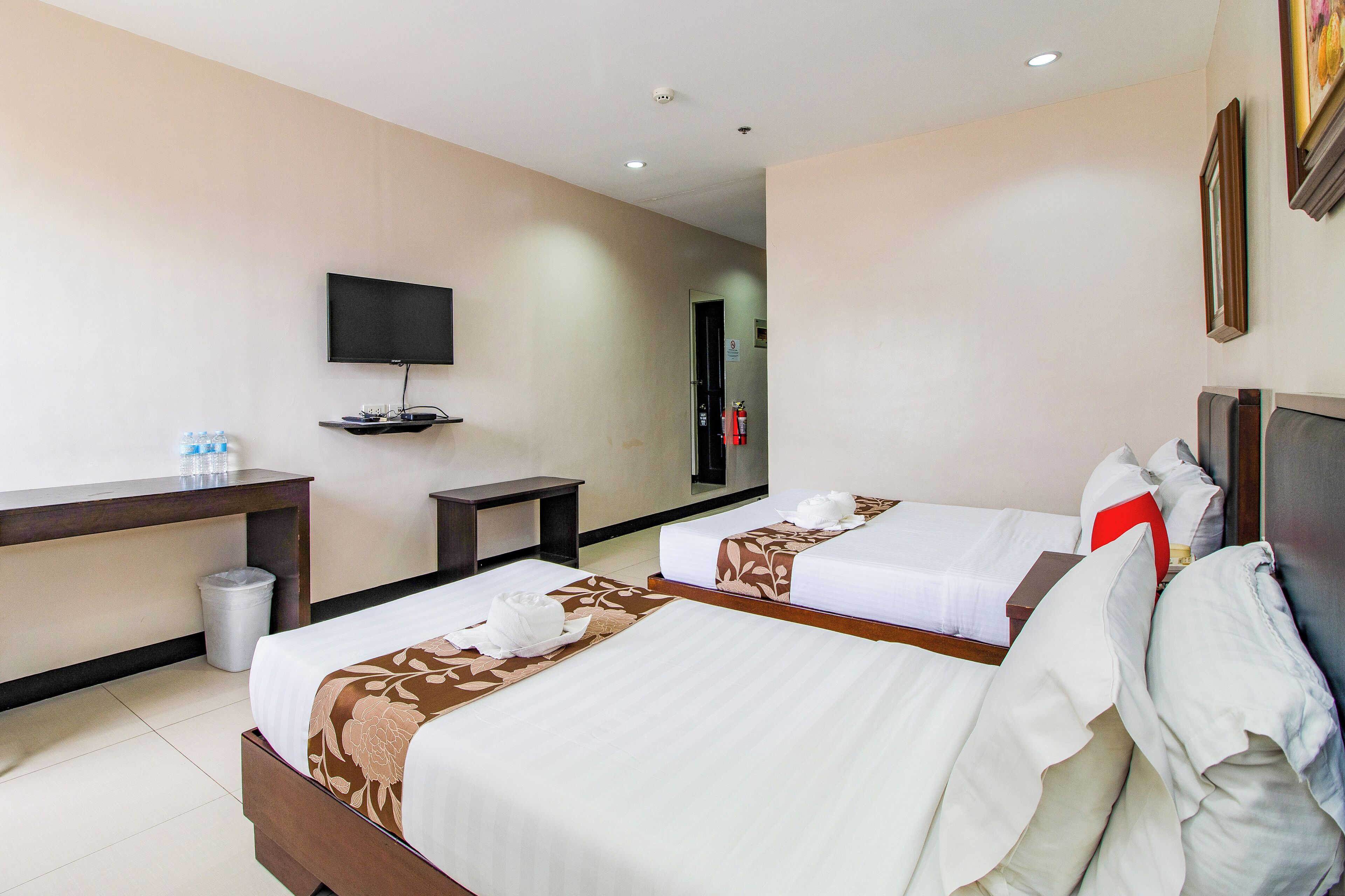 A hotel room with two beds, a TV, a desk, and a trash bin.