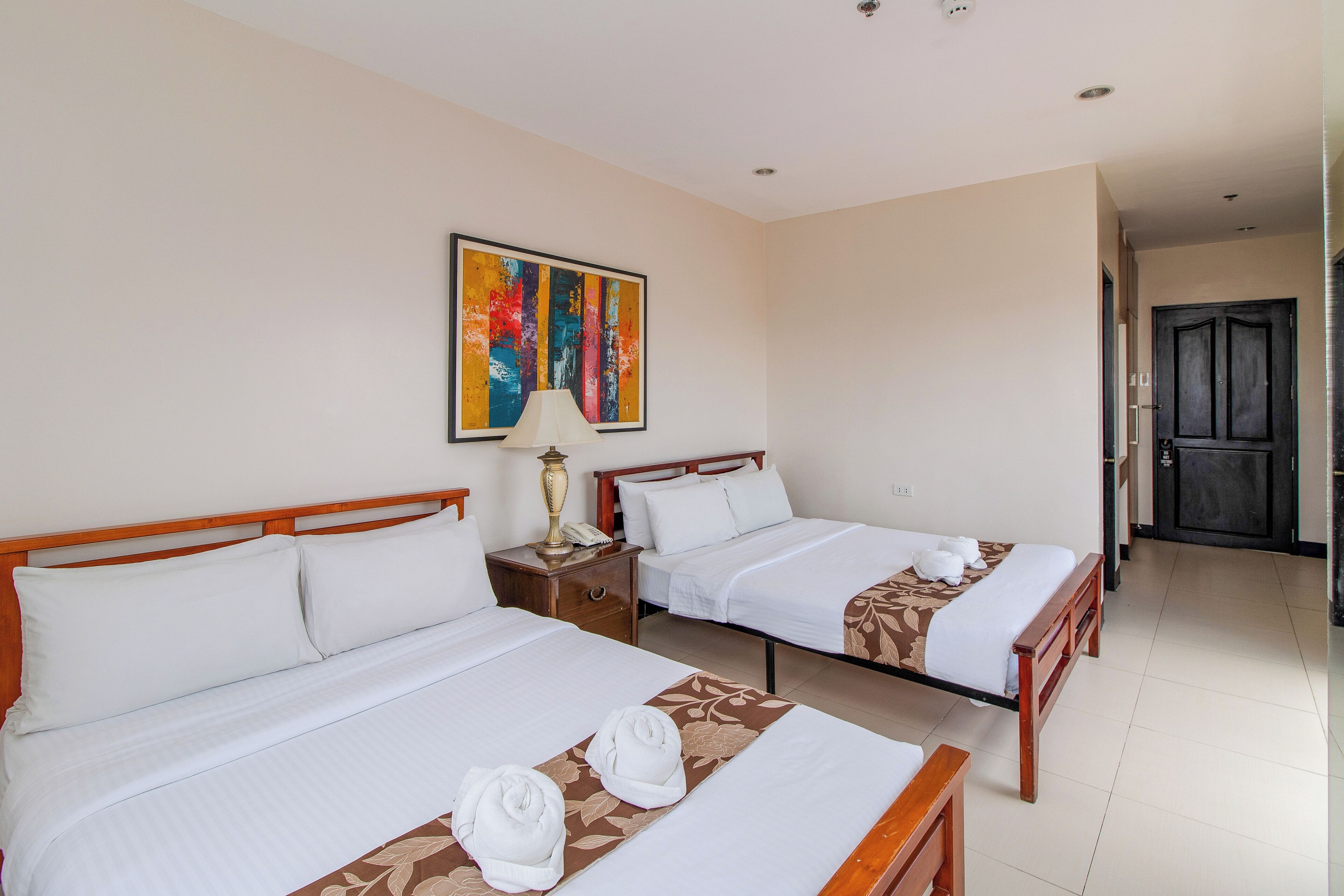 Habitación de hotel con dos camas, un cuadro en la pared, una lámpara y una puerta que da a otra habitación.