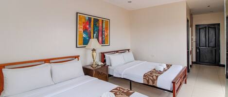Habitación de hotel con dos camas, un cuadro en la pared, una lámpara y una puerta que da a otra habitación.