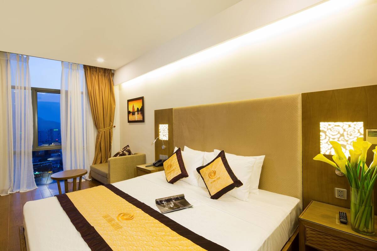 A hotel room with a large bed, a nightstand, a chair, a small table, and a window with curtains.