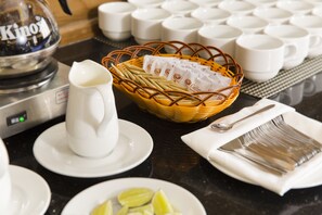 Une table avec une machine à café, un panier de sachets de thé, un pichet et une assiette de quartiers de citron.