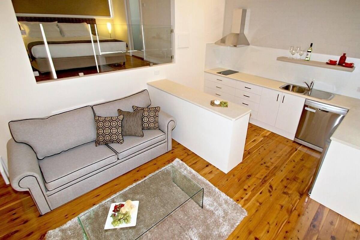 Un espace de vie compact comprenant un canapé, une petite table basse, un coin cuisine avec un lave-vaisselle et une fenêtre donnant sur l’intérieur.