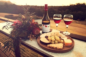 A wooden board with cheese, grapes, and a bottle of wine on a terrace overlooking a scenic landscape. - Wine Country Villas (Pokolbin)