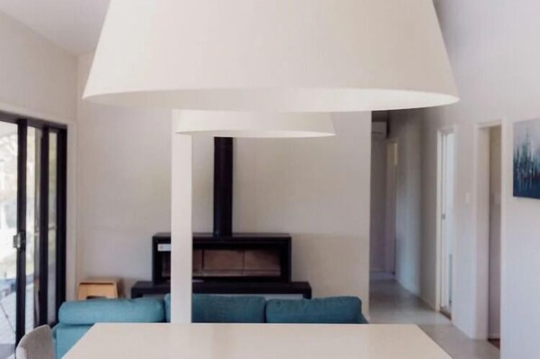 A modern living room with a white table, blue sofas, a black fireplace, and a large white ceiling lamp. - Wine Country Villas (Pokolbin)