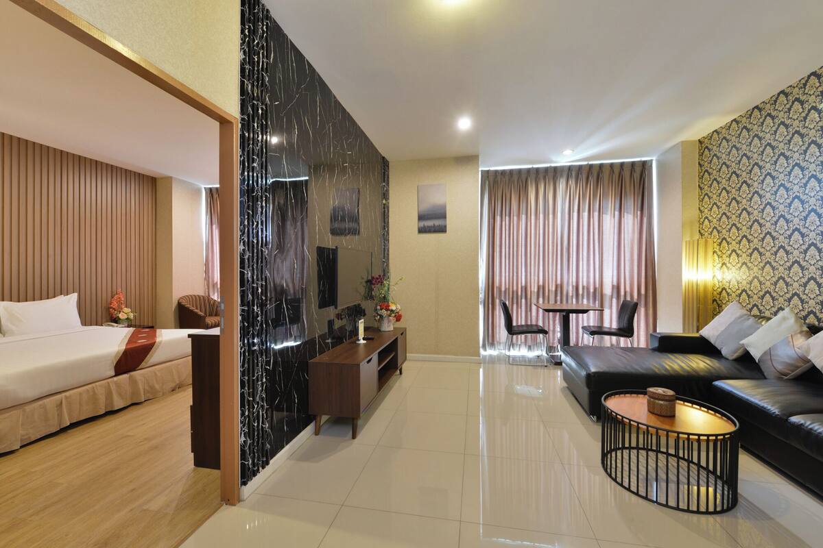 A modern hotel room with a bed, a sofa, a dining area, and a living area.