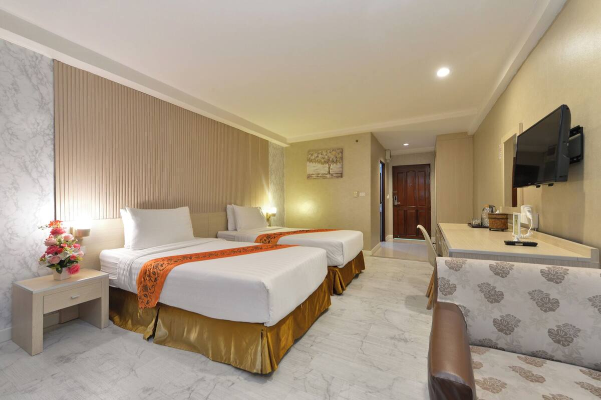 A hotel room with two beds, a desk, a chair, a TV, and a bathroom.