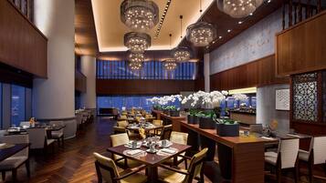 A spacious restaurant with multiple dining tables and chairs, large windows, and decorative hanging lights.