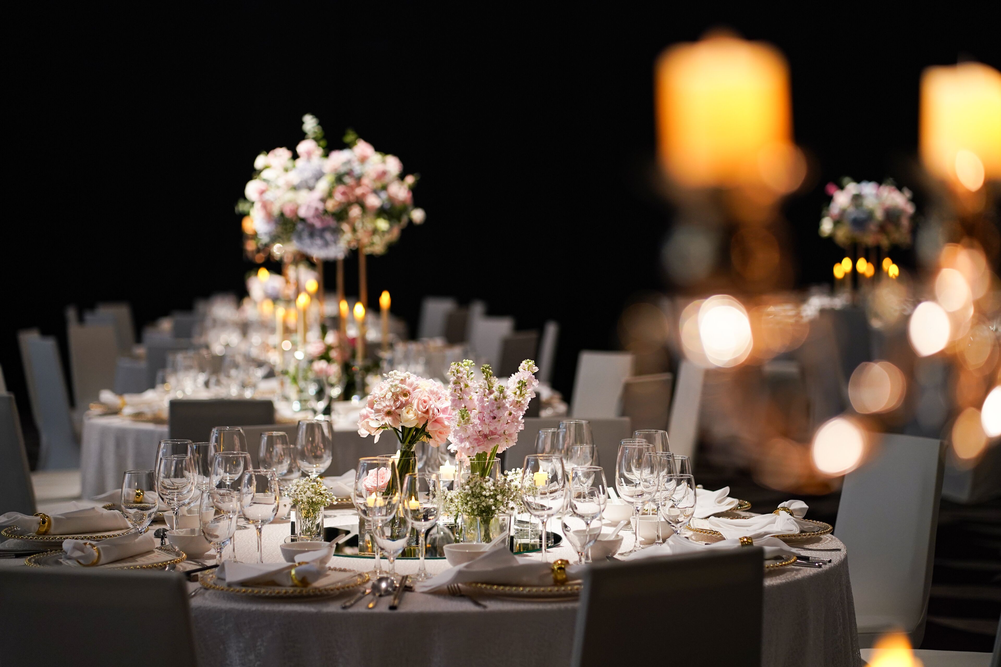 A formal dining setup with multiple tables, each set with white tablecloths, glassware, and floral centerpieces.
