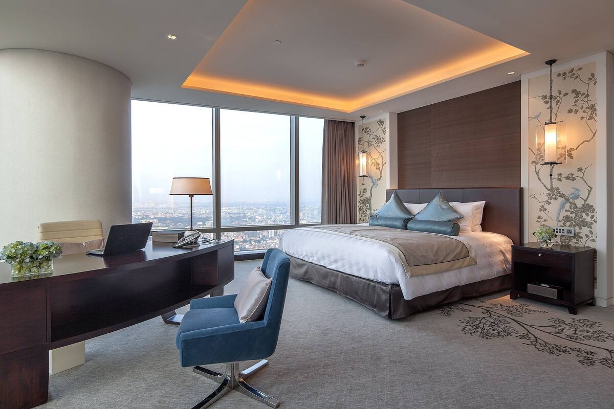 A modern hotel room with a large bed, a desk, and a view of the city.