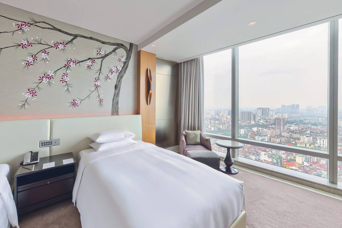 A hotel room with two beds, a city view, a wall mural, and a cityscape visible through large windows.