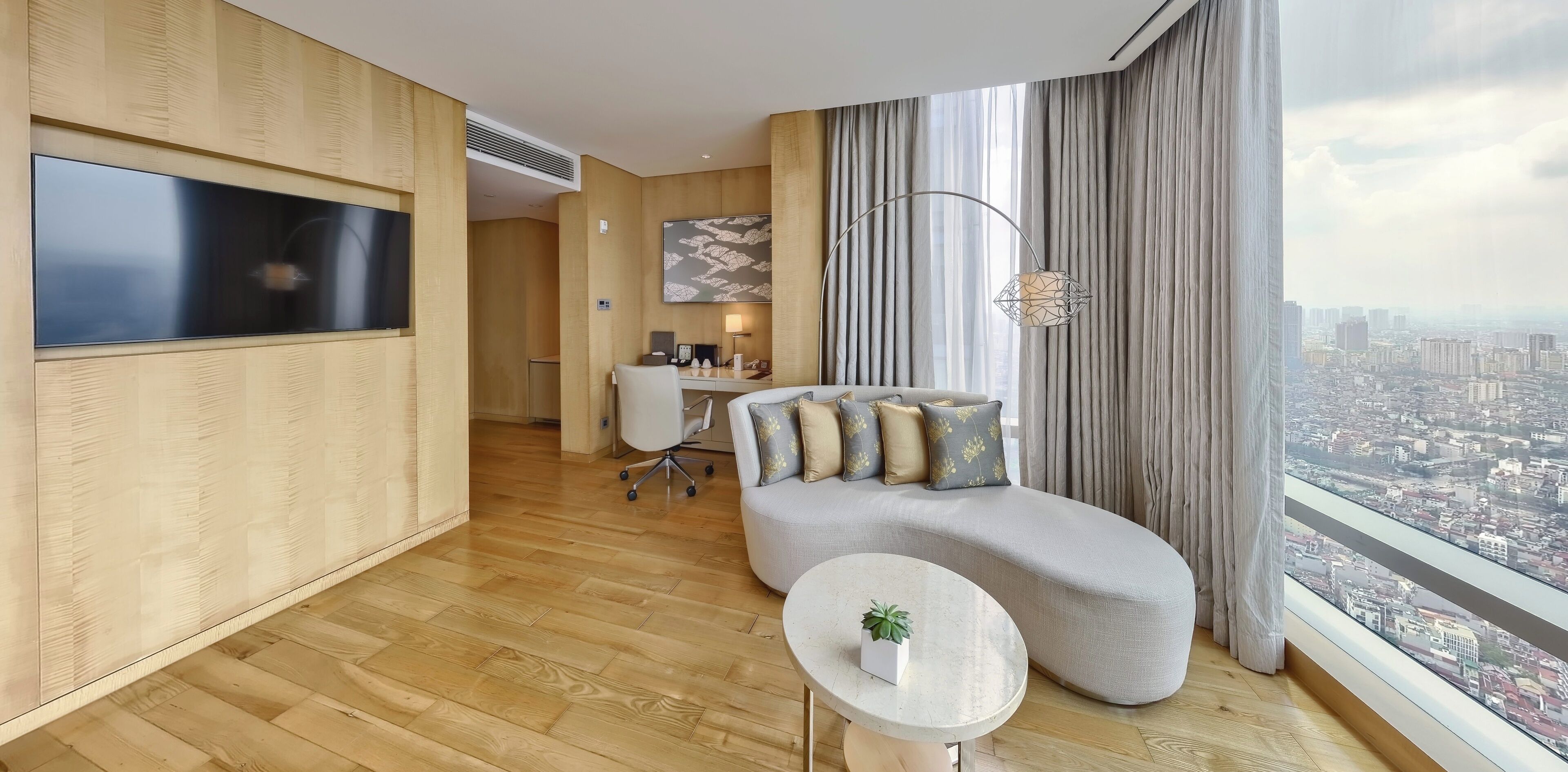 A modern hotel room with a large TV, a sofa, a small table with a plant, and a city view.