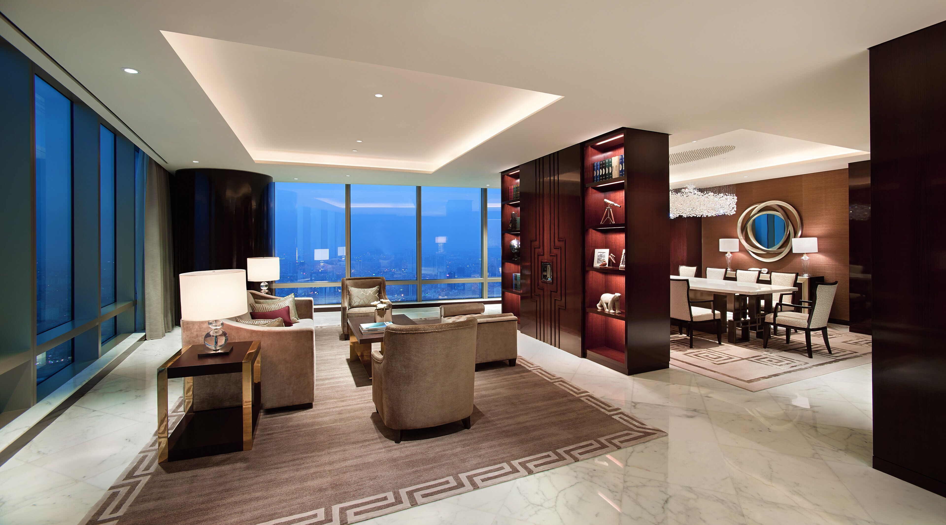 A modern hotel room with a large city view, a dining area, and a bookshelf.