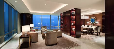 A modern hotel room with a large city view, a dining area, and a bookshelf.