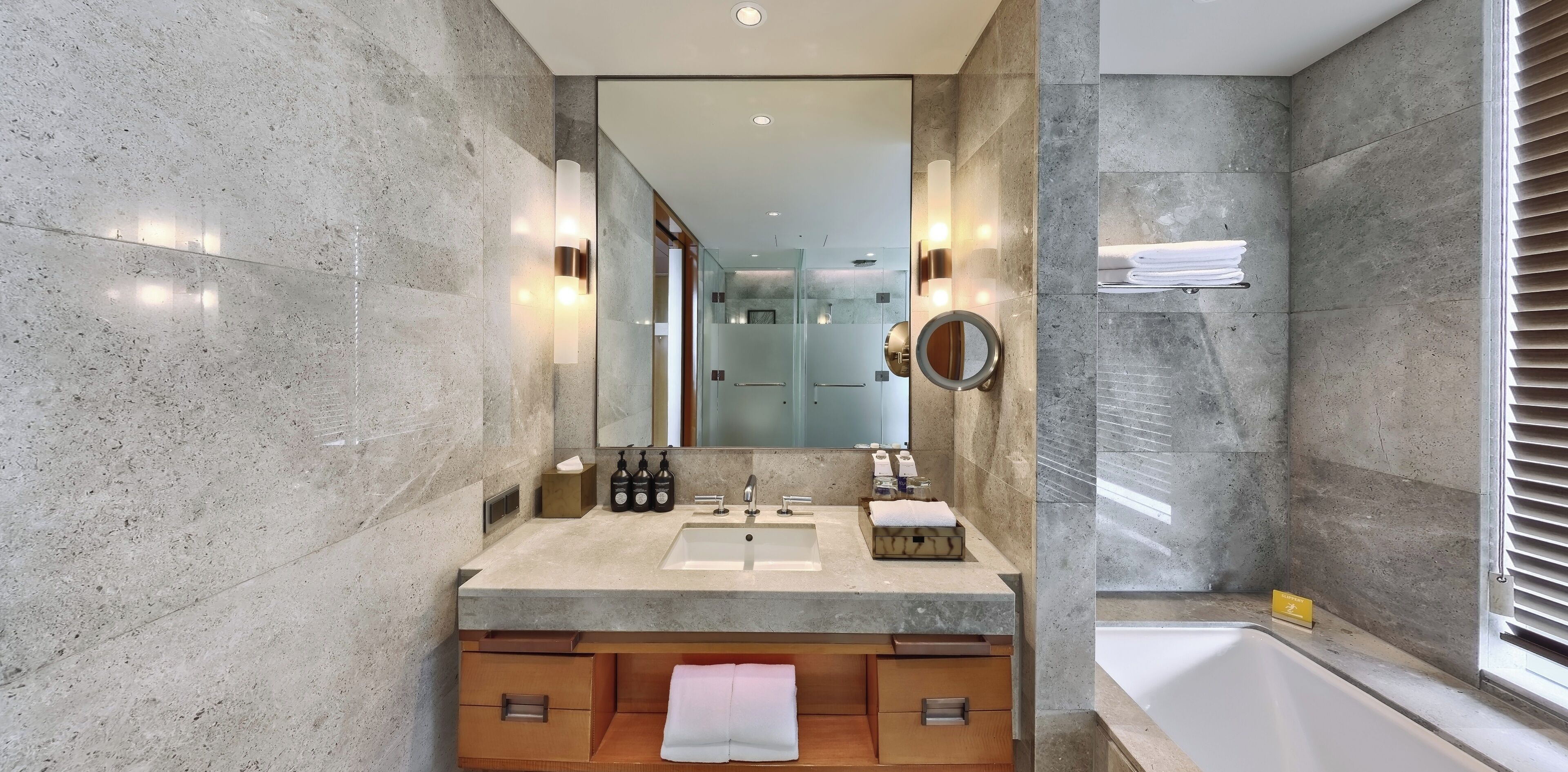 A modern bathroom with a large mirror, two sinks, a bathtub, and a vanity with drawers.