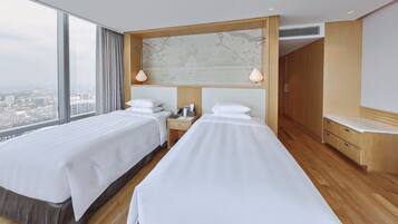 Quarto de hotel com duas camas, um guarda-roupa de madeira, uma mesa de cabeceira e vista para a cidade.