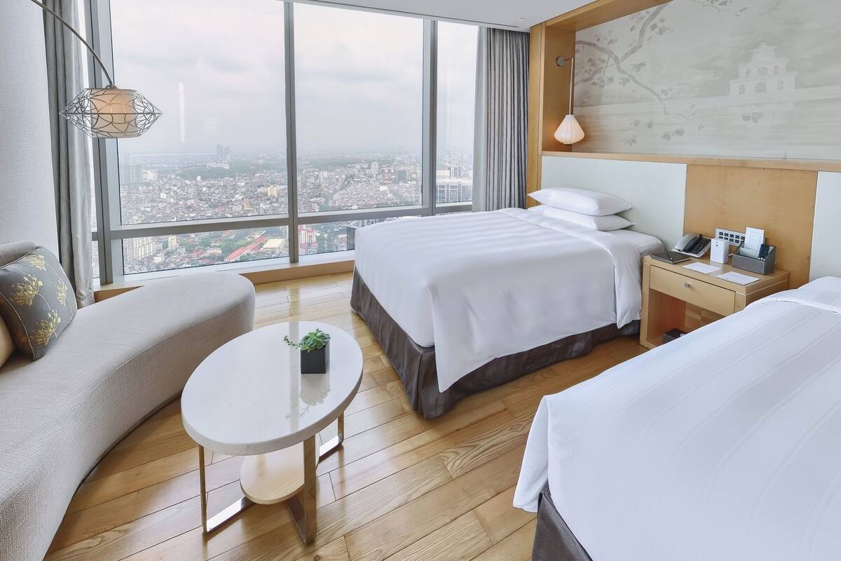 A hotel room with two beds, a sofa, a small table, and a view of the city.