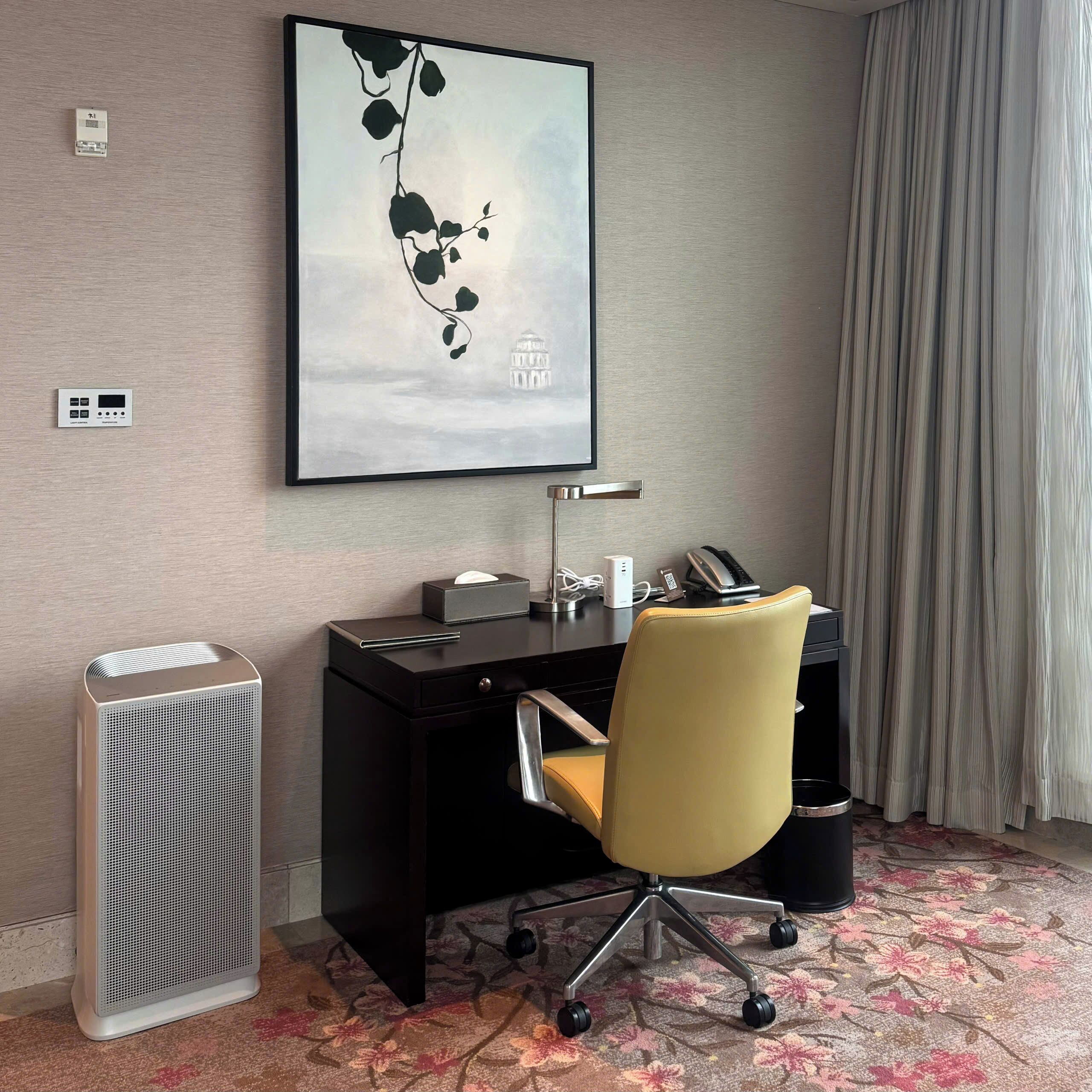 Habitación de hotel con escritorio, silla y una obra de arte enmarcada en la pared.