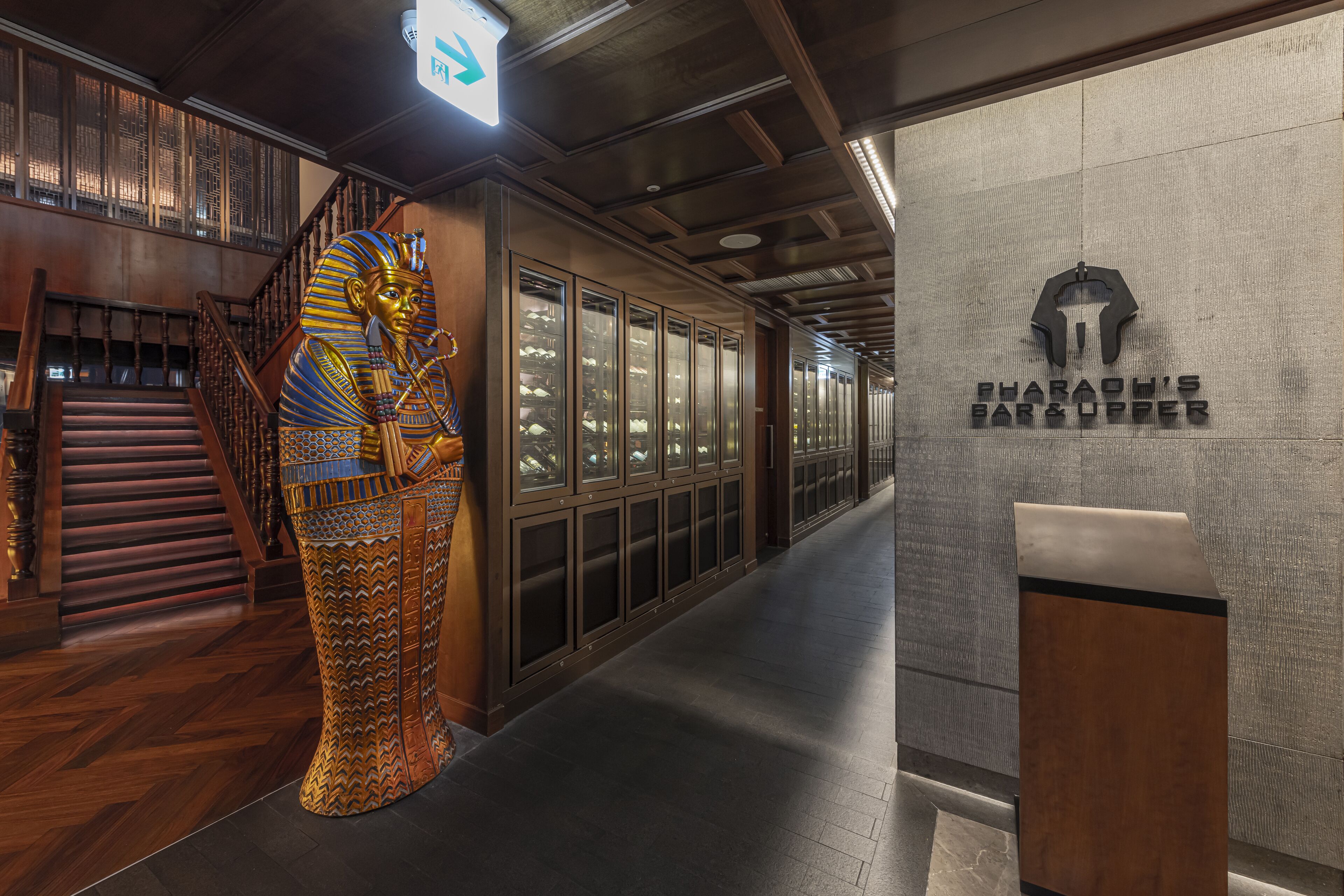 A modern interior with a large golden statue of an Egyptian figure, a staircase, and a wall with a logo for "RAHMOND'S BAR & DINE".