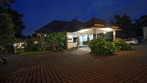 A modern building with a covered entrance, paved driveway, and surrounding greenery. - The Brothers Villas Padang Padang (Pecatu)