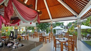 An outdoor restaurant area with wooden tables and chairs, a bar counter, and a covered seating area with a view of the surrounding landscape. - The Brothers Villas Padang Padang (Pecatu)