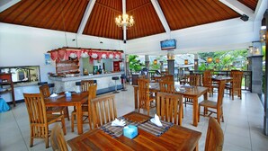 A spacious indoor dining area with wooden tables and chairs, a central bar area, and a view of greenery outside. - The Brothers Villas Padang Padang (Pecatu)