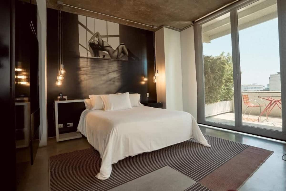 Un dormitorio moderno con una cama grande, una mesita de noche y vistas al exterior a través de un ventanal corredero.