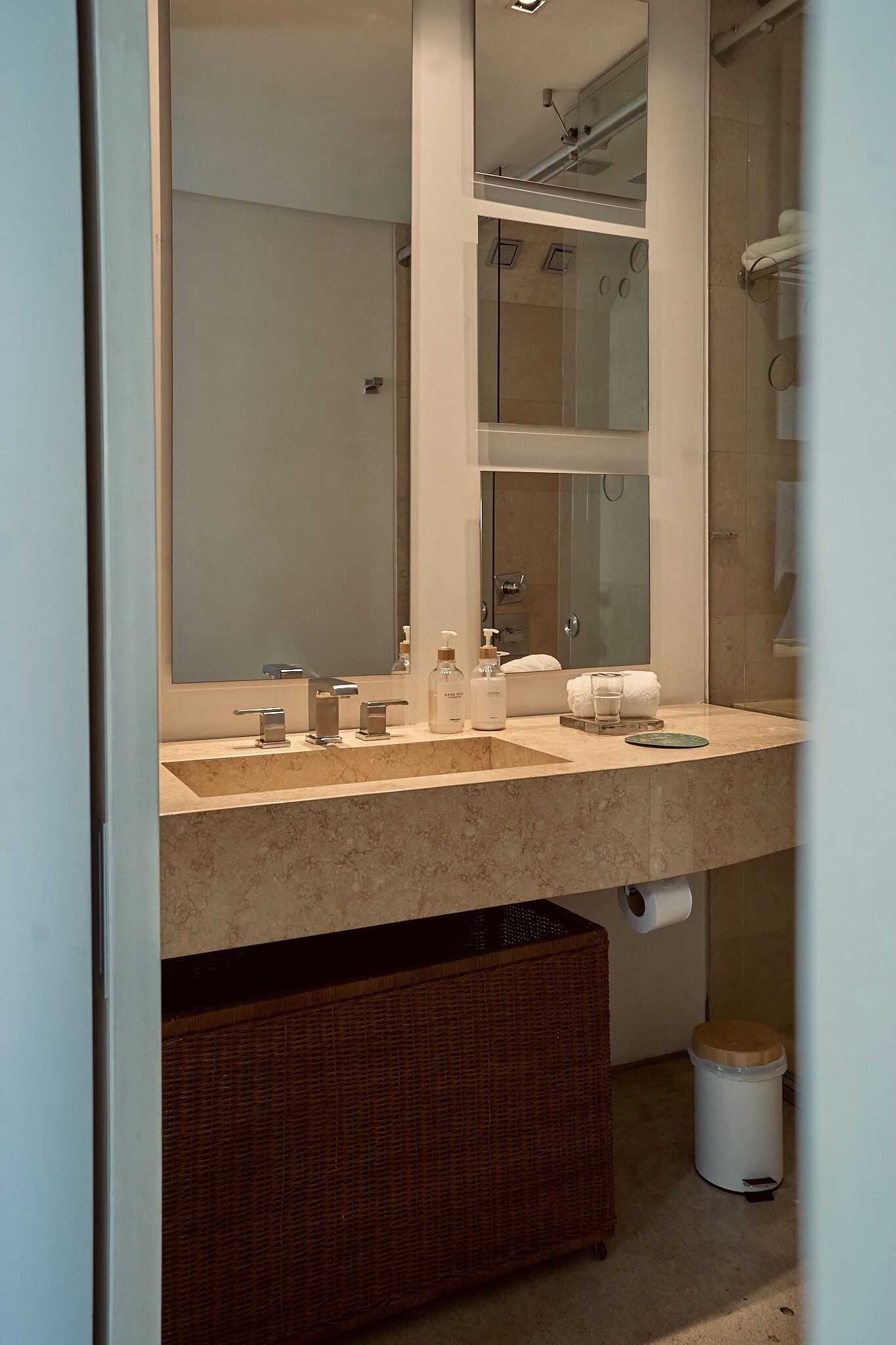 Un baño moderno con un espejo grande, dos lavamanos, una ducha y una cesta de mimbre.