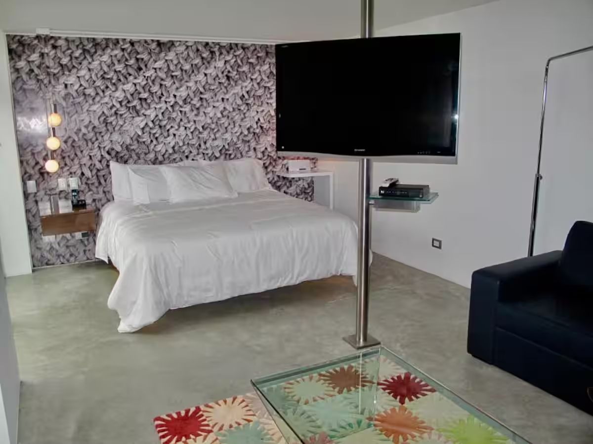 A bedroom with a bed, a TV mounted on the wall, a small bedside table, and a sofa.