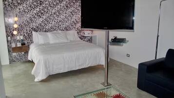 A bedroom with a bed, a TV mounted on the wall, a small bedside table, and a sofa.