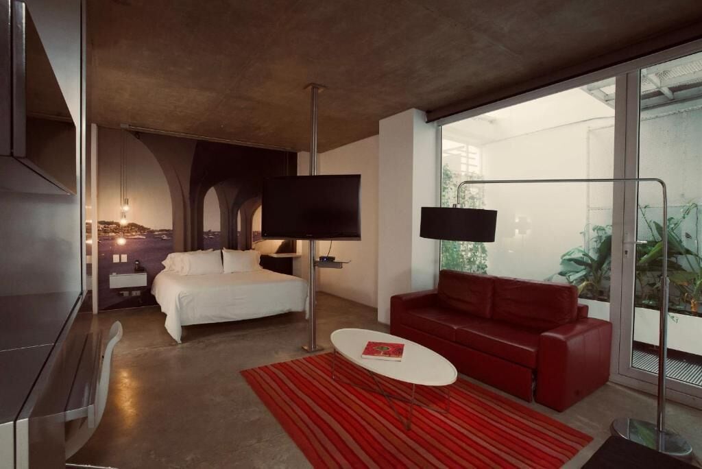 A modern hotel room with a bed, red sofa, and a TV.