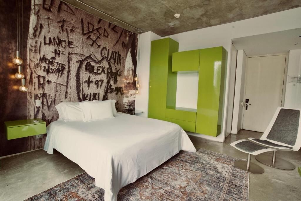 Un dormitorio moderno con una cama grande, una pared de acento verde y una silla minimalista.