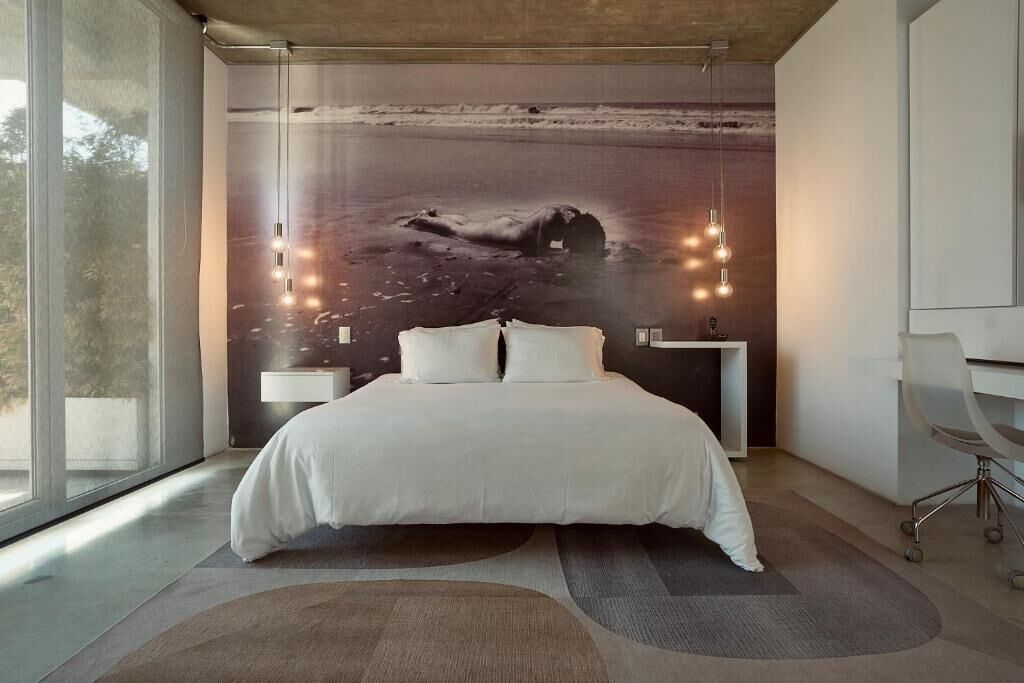 A modern bedroom with a large bed, a mural of a beach scene, and a desk with a chair.