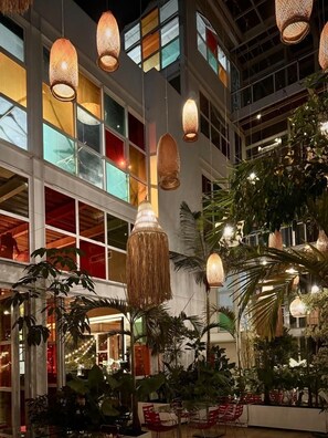 Un espacio interior moderno con lámparas de mimbre colgantes, ventanas amplias y plantas de interior.