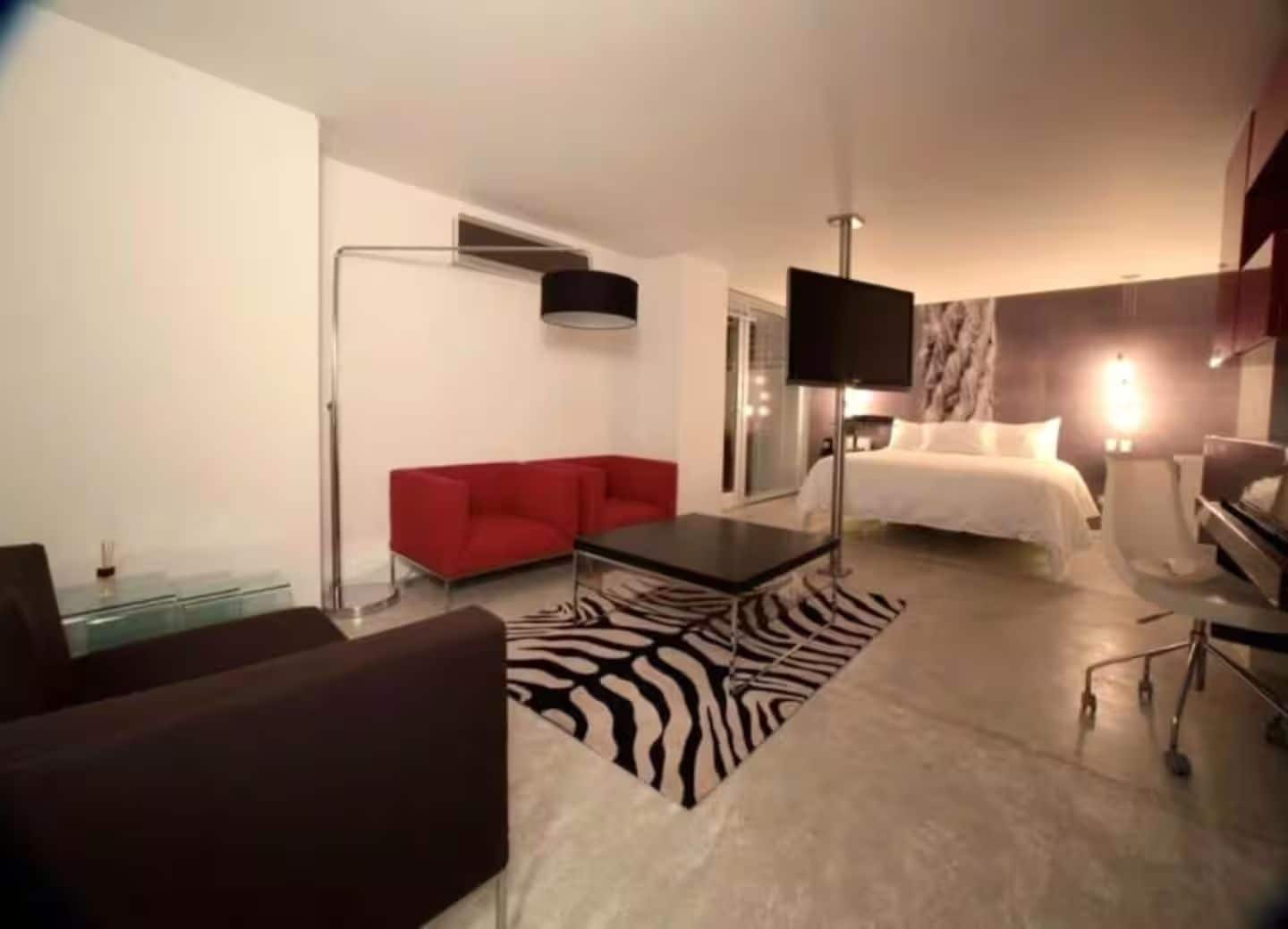 A modern hotel room with a red sofa, a flat-screen TV, a bed, and a zebra-patterned rug.