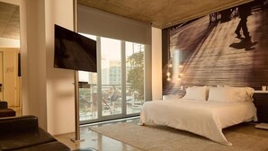 A modern hotel room with a large bed, a flat-screen TV, and a view of the city through large windows. - Now Hotel Cali - Adults Only (Cali)