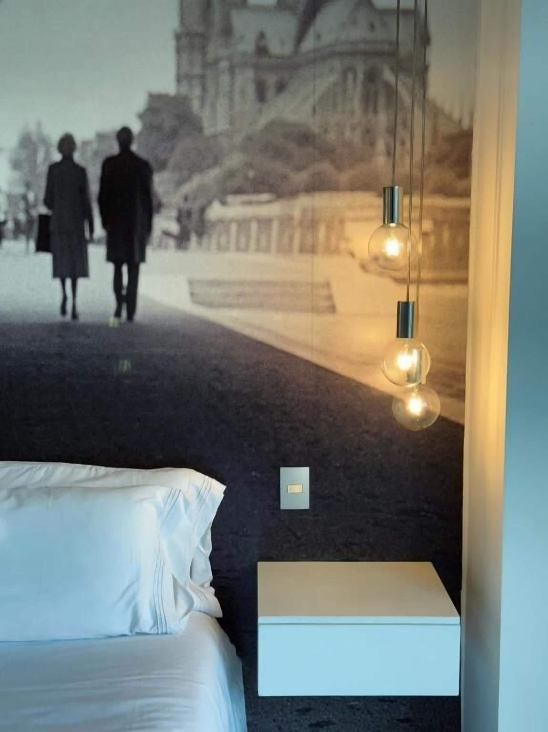 Un dormitorio con cama, mesita de noche y lámpara de pared.