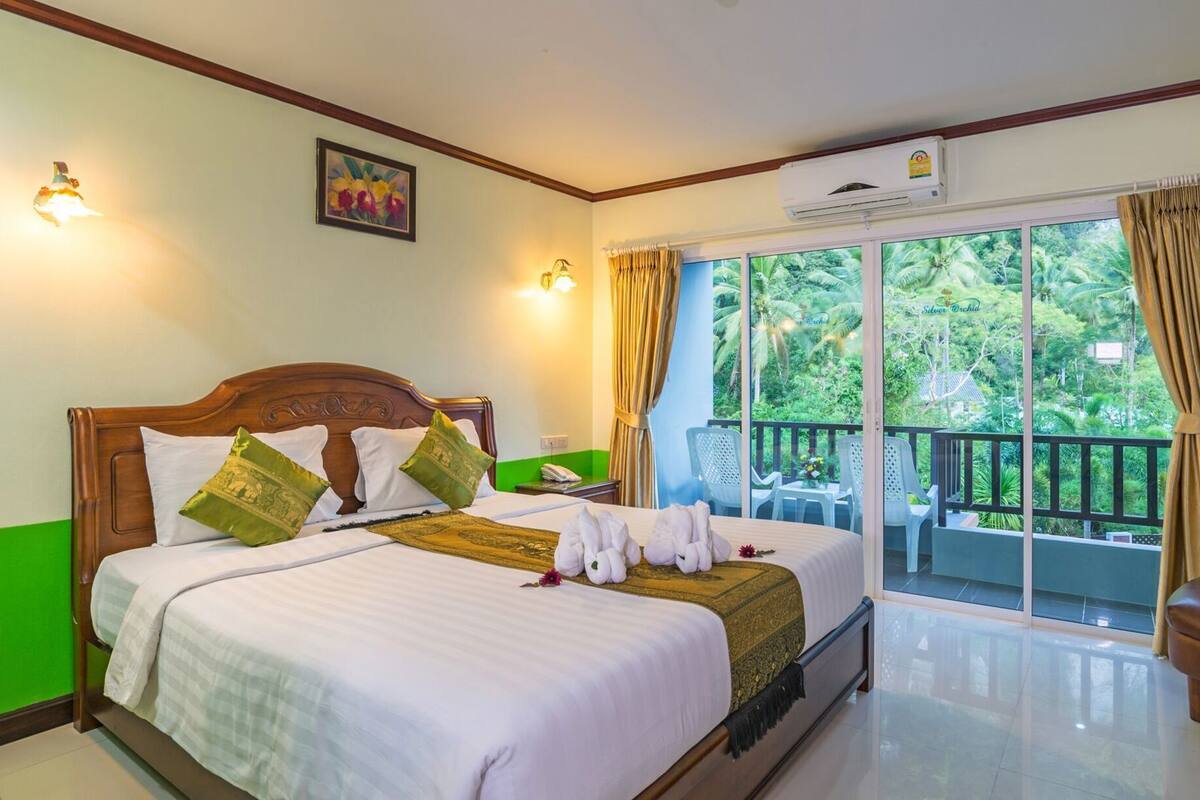 A hotel room with two beds, a balcony with a view of greenery, and an air conditioning unit.