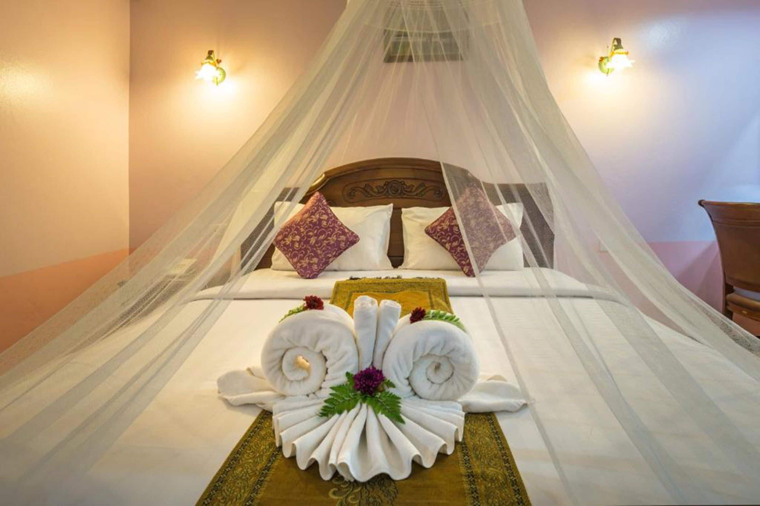 A neatly made bed with a canopy, pillows, and a decorative towel arrangement.