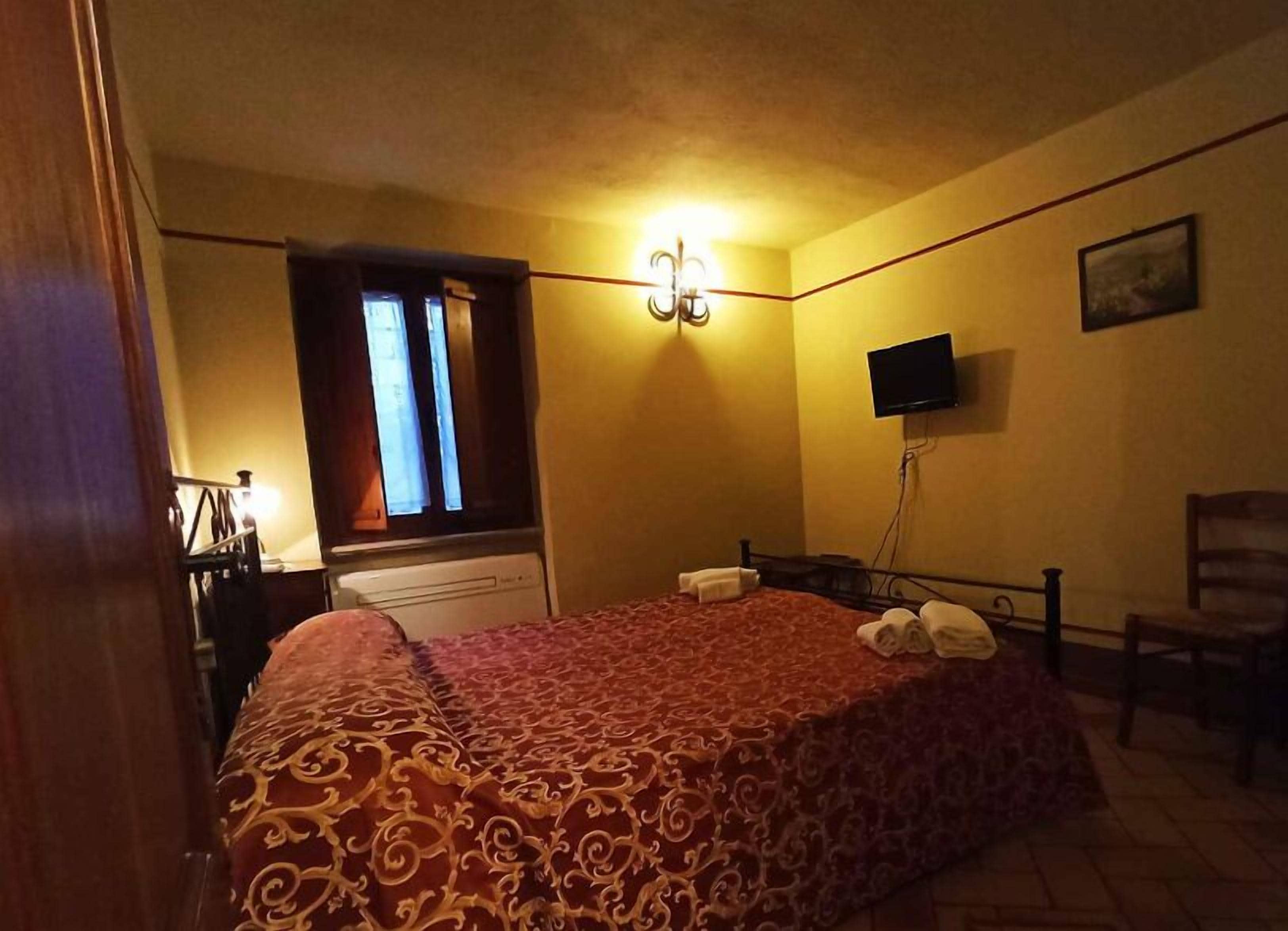 A bedroom with a bed, a television, a window with curtains, and a chair.
