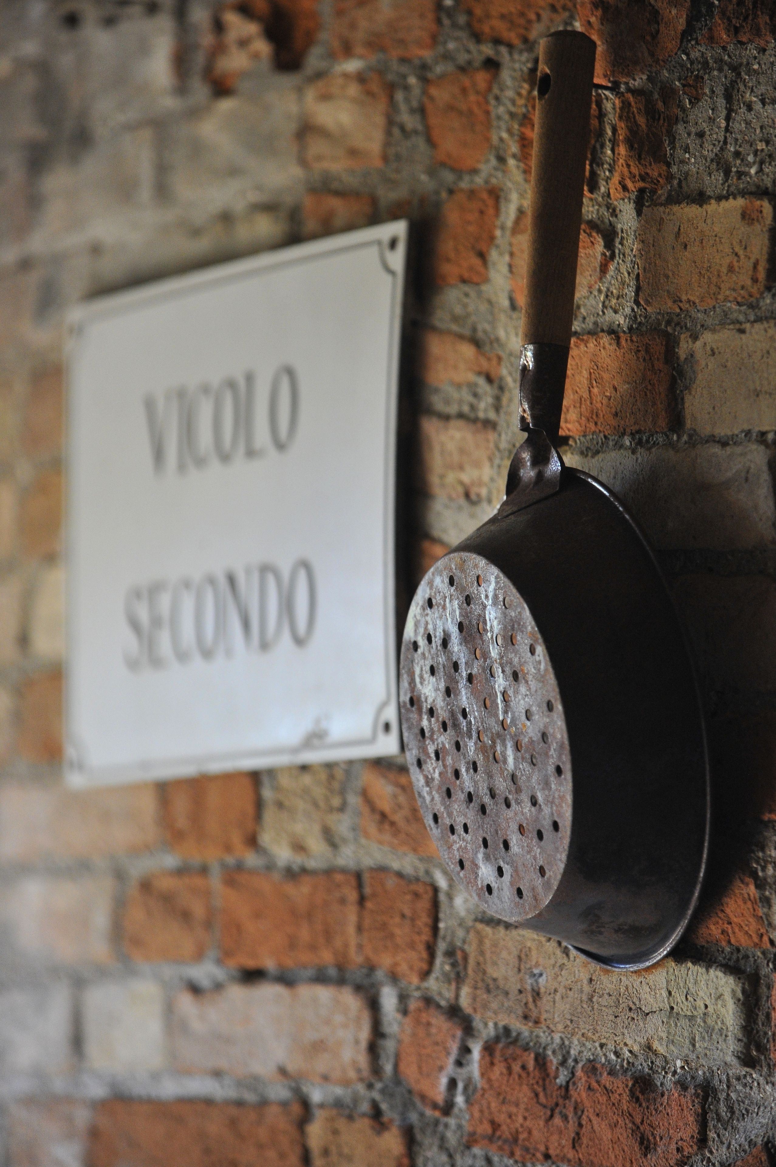 A metal bucket with holes, mounted on a brick wall, and a sign reading "VICULO SEGUNDO".