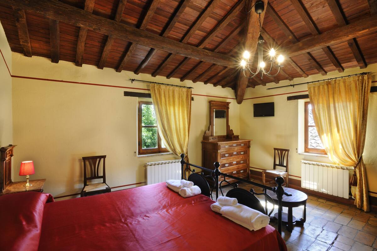 Ein Zimmer mit Holzboden, einem Bett mit roter Bettwäsche, einem Holzschrank und einem Stuhl.