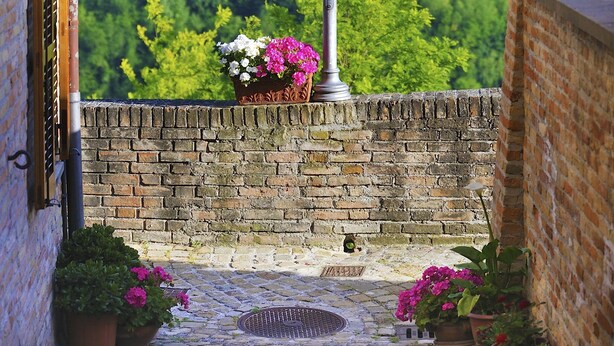 A brick wall with a metal grate, potted plants, and a street lamp overlooking a green landscape. - Albergo Diffuso Borgo Montemaggiore (Colli al Metauro)