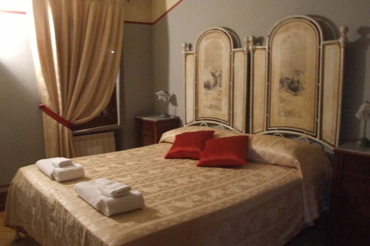 Ein Hotelzimmer mit einem großen Bett, einem Nachttisch, einer Lampe und einem Fenster mit Vorhängen.