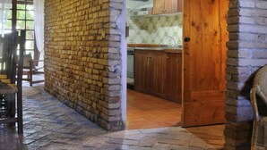 A rustic interior with exposed wooden beams, a stone wall, and a wooden door leading to a kitchen area. - Albergo Diffuso Borgo Montemaggiore (Colli al Metauro)
