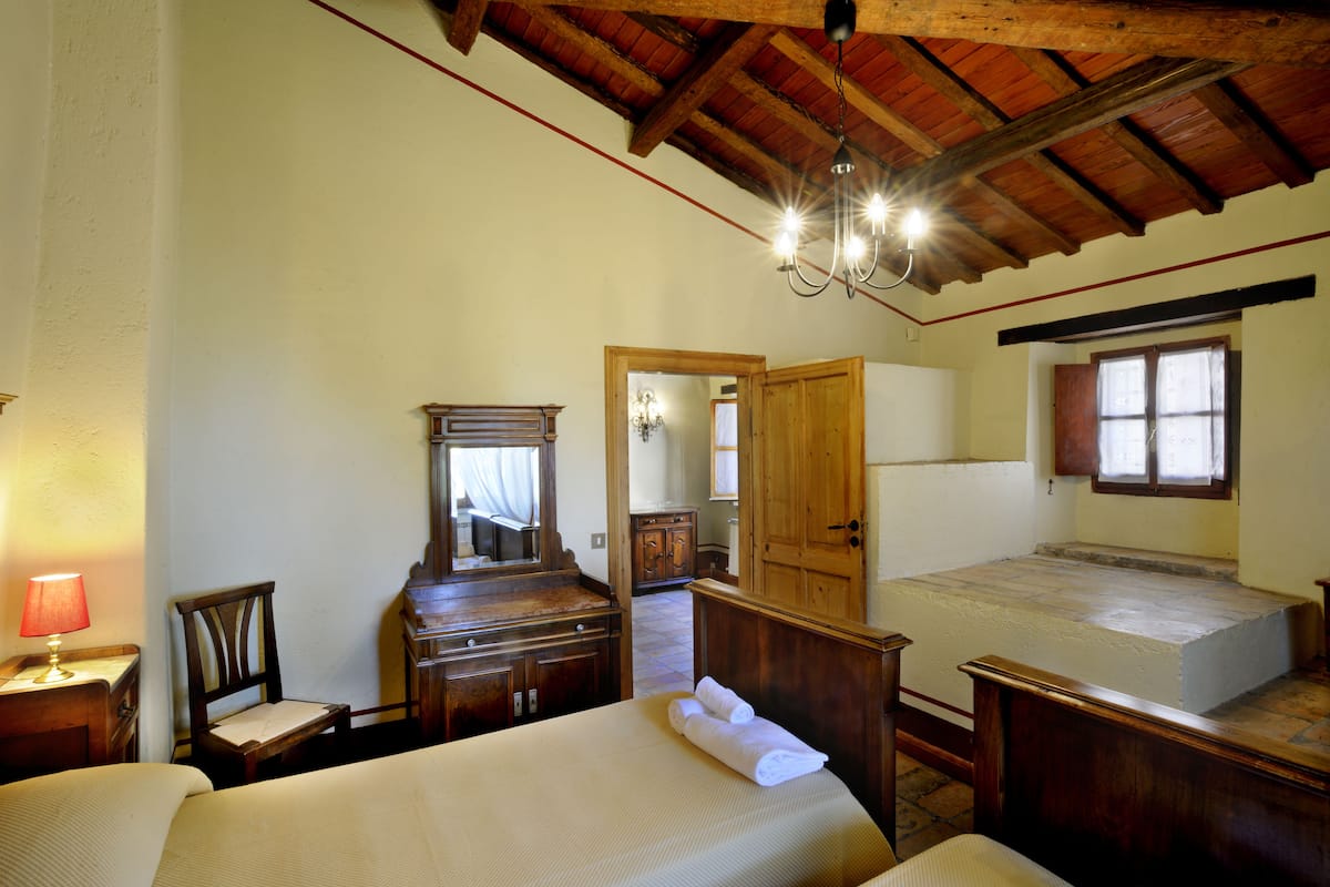 Ein Schlafzimmer mit Holzbalkendecke, einem Bett, einer Kommode, einem Stuhl und einem Spiegel.