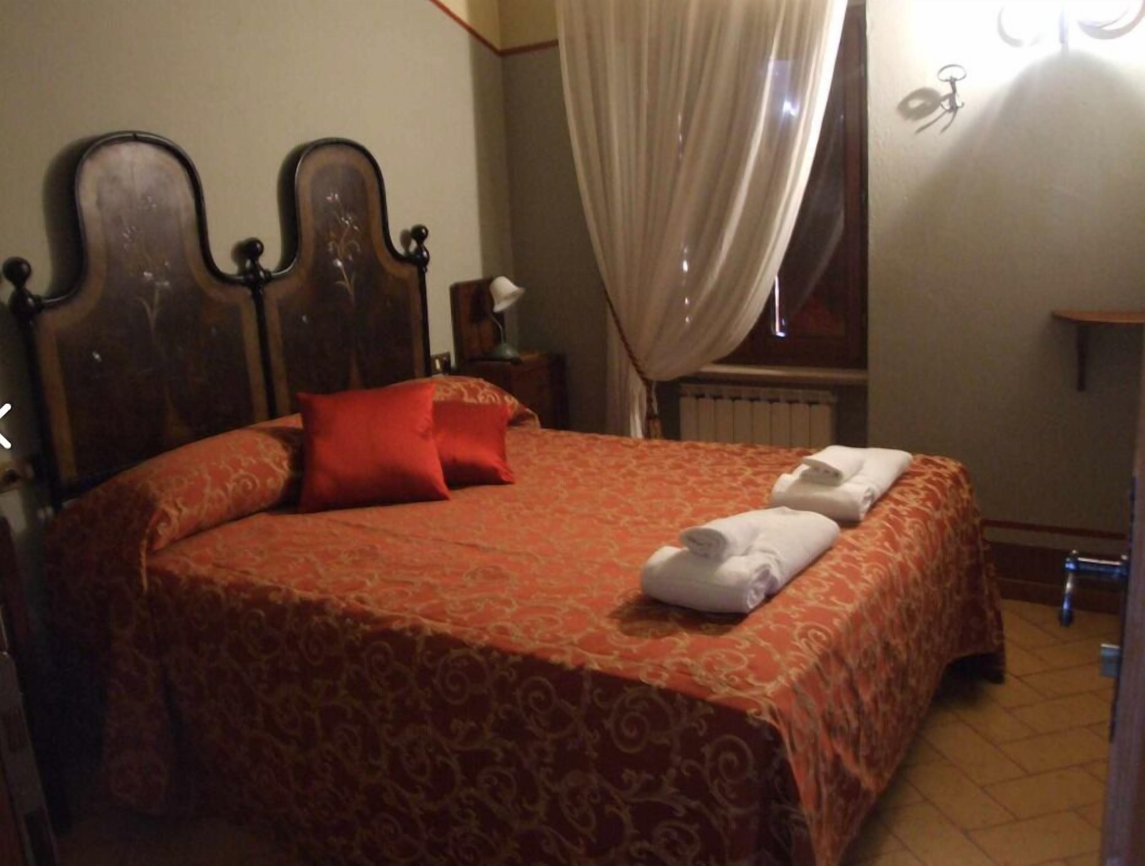 A neatly made bed with a patterned bedspread, a red pillow, and two folded towels.