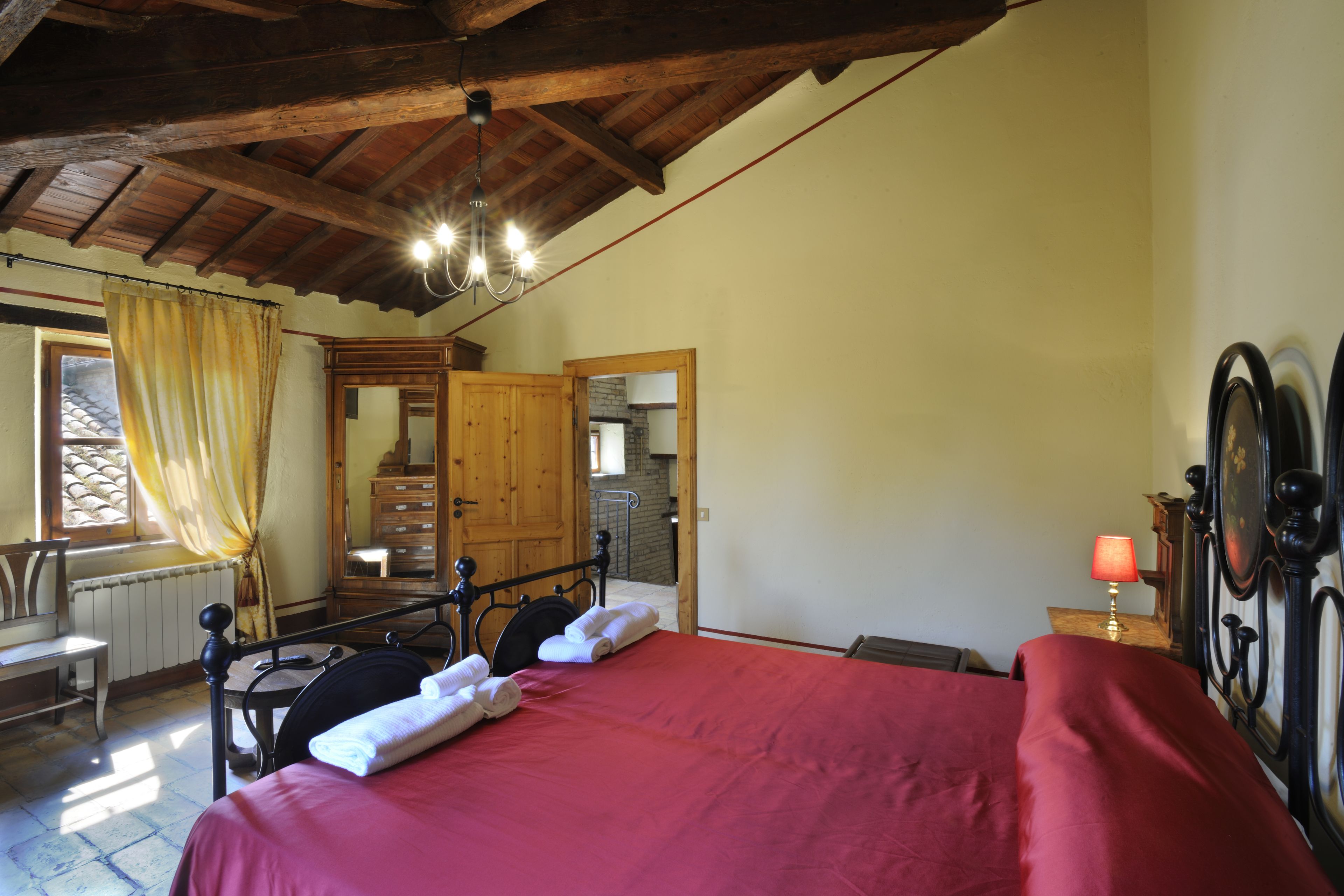 A bedroom with a wooden bed, a nightstand, a lamp, a mirror, and a window with curtains.