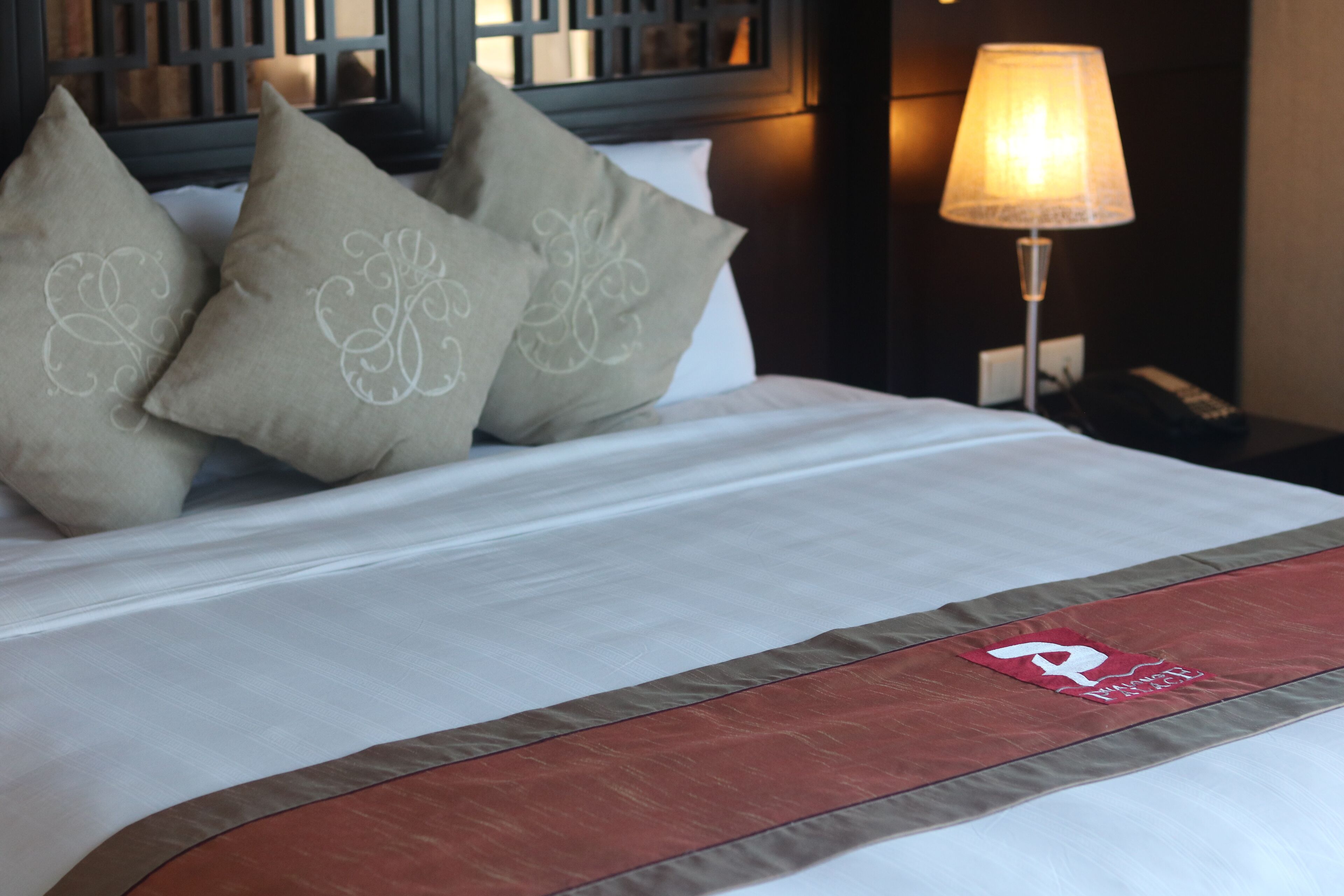 A neatly made bed with a decorative pillow and a red and brown bed runner.